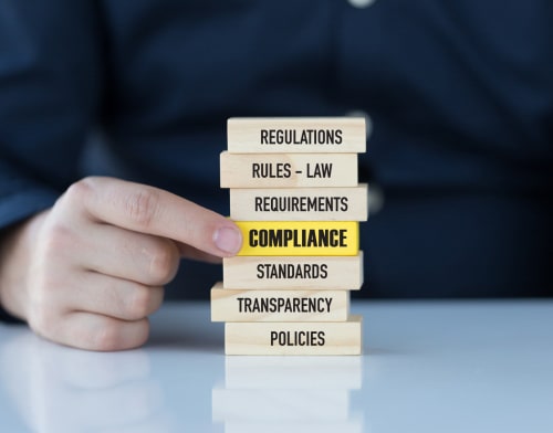 A stack of wooden blocks, with a yellow block in the middle with 'compliance' written on it