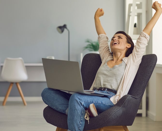 Woman sits in seat behind her laptop and cheers
