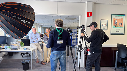 The film crew records Sven and Mireille in an office for an interview about archiving and scanning at Merak.