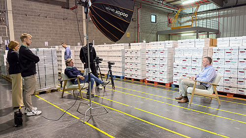 Sven is interviewed in a warehouse with archive boxes, while the film crew captures the conversation.